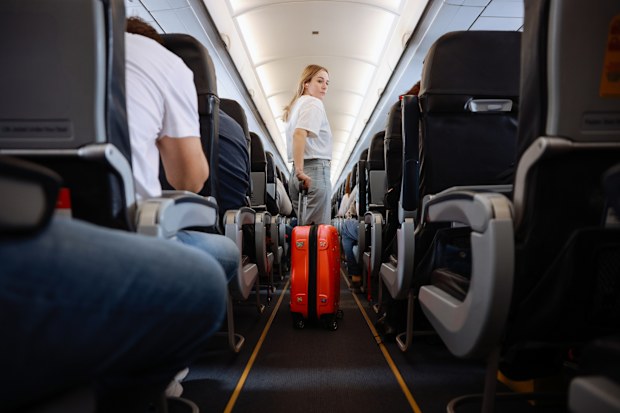 Interior of airplane with people sitting on seats. Passengers with suitcase in aisle looking for seat during flight.