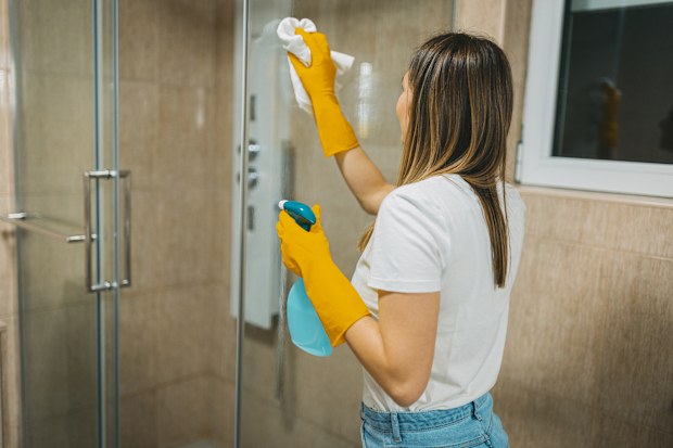 A woman polishing a front side of the shower. Clean and shiny glass.