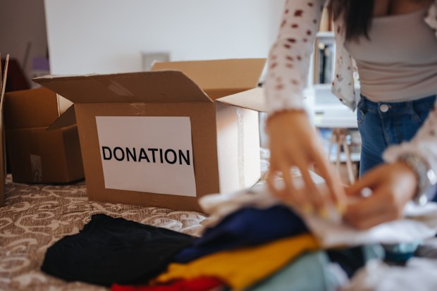 Beautiful young woman packing clothes in donation boxes at home