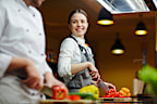 Smiling trainee talking to expert while cutting raw pepper�
