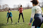 A diverse group of women exercising, jumping in the air doing burpees in a public park surrounded by nature. They are working out in their community to get exercise and spend quality time together.