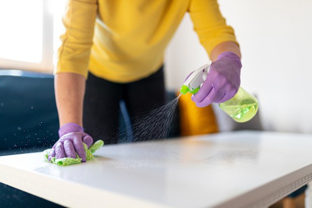 Midsection of a woman with protective gloves holding spray bottle and using rag to disinfect coffee table in the living room against viruses