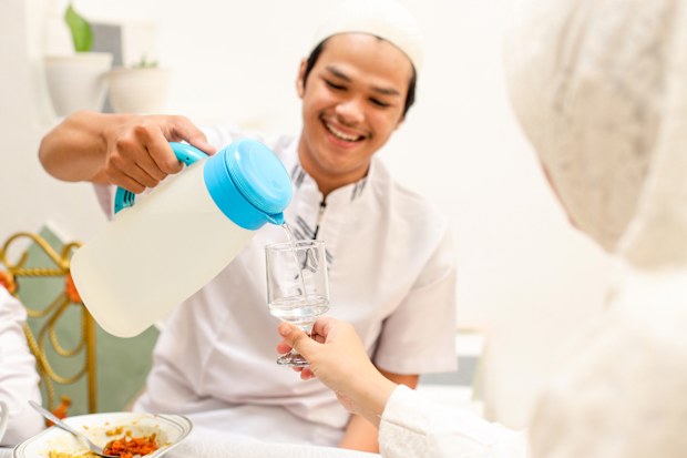 Young Man Pouring Water For His Sister On Eid Dinner Celebration