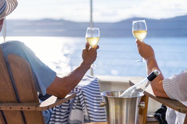 Couple relaxing and drinking wine on deck chairs in an over water bungalow. They are looking at the view