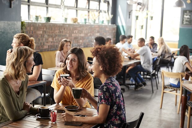 Three Young Female Friends Meeting Sit At Table In Coffee Shop And Talk