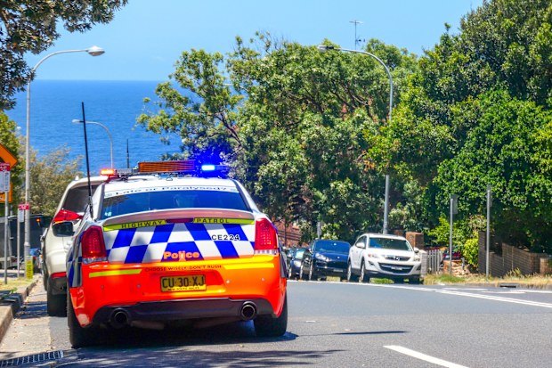 An officer of the NSW Police Highway Patrol has pulled over the driver of a vehicle on Bondi Road, Bondi. The police officer has parked his car behind the stopped vehicle and leaves the emergency lights flashing.  In the distance is the Pacific Ocean.  This image was taken in the afternoon on 3 January 2023.