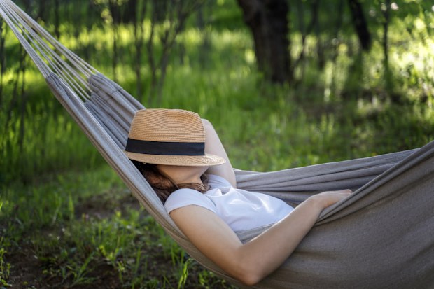 Woman resting in a hammock in a summer garden covering her face with a straw hat. Summer vacation concept