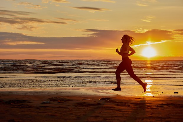 Active woman in sportswear is running on beach during sunset.