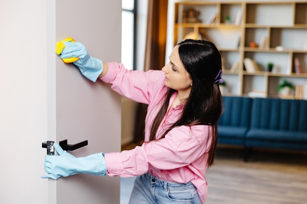 A young woman in rubber gloves wipes the door with a rag.