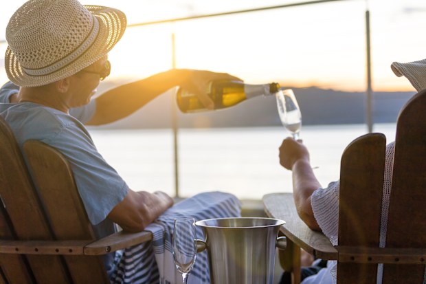 Man pouring his partner a glass of champagne at sunset. They are on the waterfront.