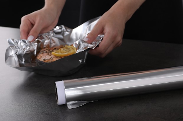 Aluminum foil and woman with tasty salmon at grey textured table, closeup