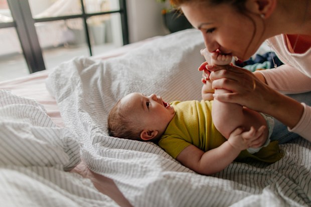 Happy baby with their mum laying on a bed playing