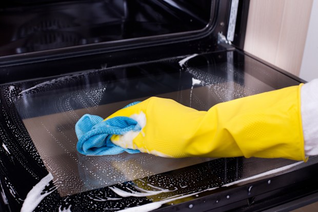 Close up of female hand with yellow protective gloves cleaning oven door