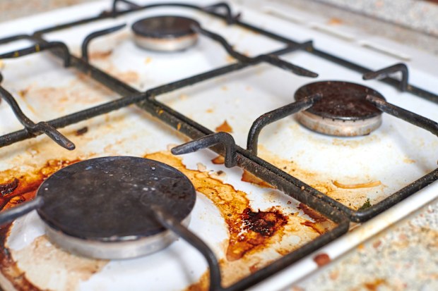 Dirty grease stove with food leftovers. Unclean gas kitchen cooktop with greasy spots, old fat stains, fry spots and oil splatters.