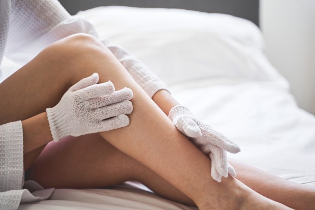 Cropped photo of a young woman in a waffle bathrobe doing dry brushing in bed