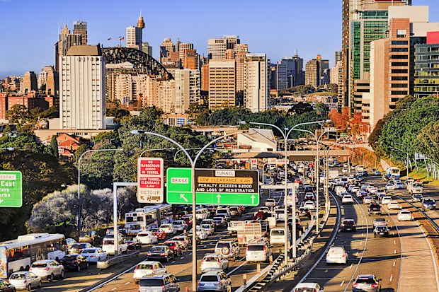 Heavy vehicles crowded Warringah freeway in North Sydney business district queing towards city harbour bridge between high rise towers and office buildings on a sunny morning.