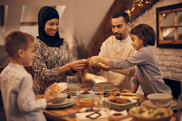 Happy Middle Eastern family sharing pita bread at dining table on Ramadan during iftar.