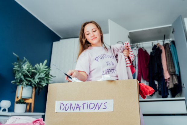 A cardboard box of selected clothes for donating to a Charity shop standing on the bed. Decluttering, Sorting clothes, and Cleaning Up. Reuse, second-hand. Conscious consumer, sustainability