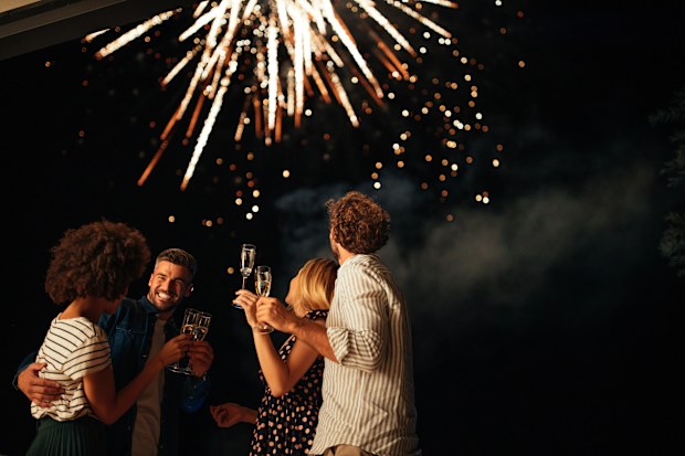 New Year's party Four friends standing outside, toasting with glasses of wine and watching fireworks