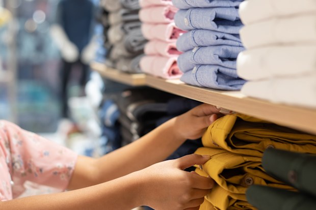 Selective focus on garments arranged in racks and human hand in a shopping mall