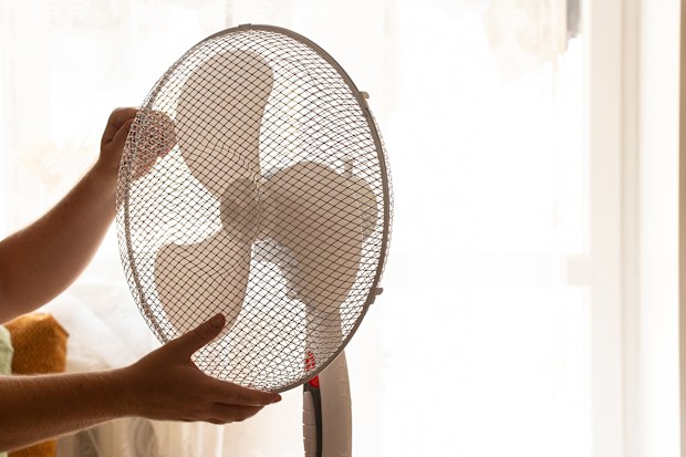 Man holding floor fan with hands at home in bedroom on hot day in summer