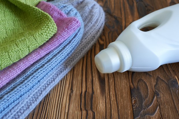 Knitted sweaters and a bottle of detergent on a wooden background