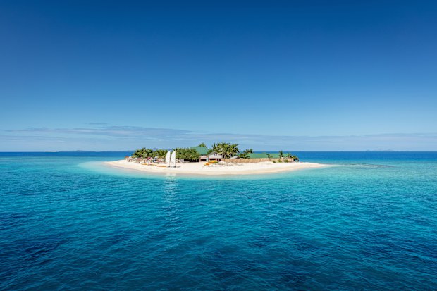 Beautiful small island in the middle of the south pacific ocean with beach huts, lounge chairs, palm trees, surrounded with beautiful clear turquoise water. Islet, Mamanuca Islands, Fiji, Melanesia