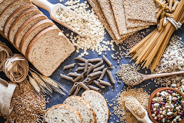 Top view of wholegrain and cereal composition shot on rustic wooden table. This type of food is rich of fiber and is ideal for dieting. The composition includes wholegrain sliced bread, wholegrain pasta, oat flakes, flax seed, brown rice, mixed beans, wholegrain crackers and spelt. 