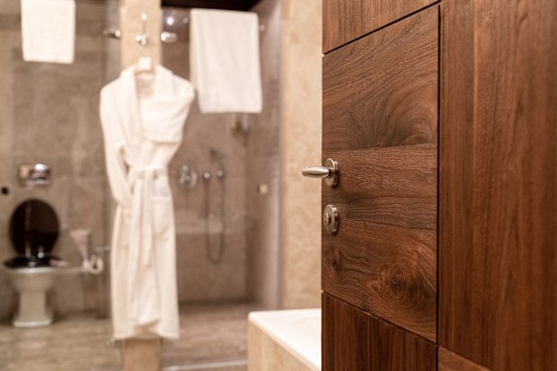 Wooden door to the bathroom in  hotel or apartament. Open  door to the bathroom, where  white cotton bathrobes hang. Hotel business concept.Out of focus.