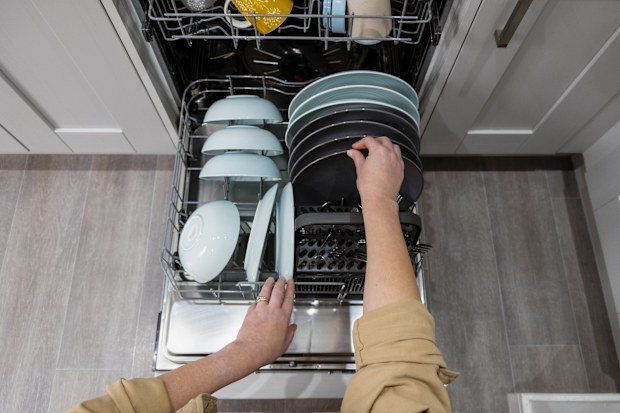 A point of view shot of an unrecognisable mature caucasian woman emptying a dishwasher full of clean crockery in her kitchen at home.