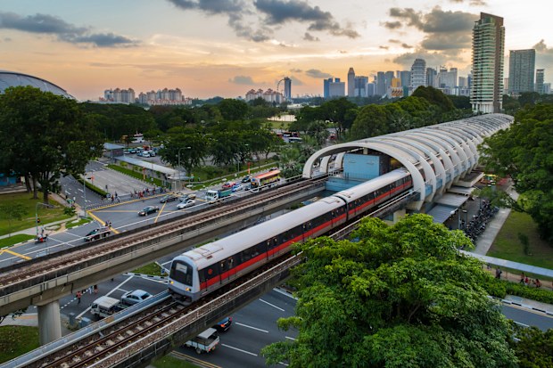 A high view point of Singapore mass rapid transit  (MRT) transportation train service in central Kallang station during sunset with Singapore city skyline in background. Singapore MRT train system serves as one of Singapore daily transportation for most commuters. Background include Singapore downtown city skyline with modern skyscrapers and commercial buildings such as Marina Bay Sands and Singapore flyer