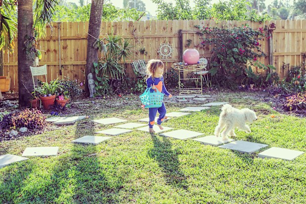 Little girl walking through a backyard with a basket and a dog