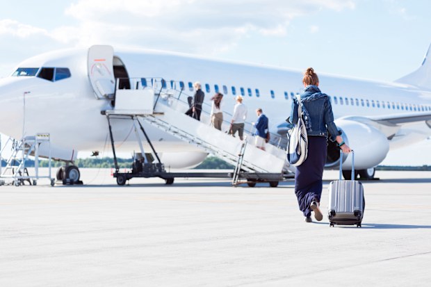 Rear view of young woman with luggage walking towards the airplane. Female traveler going on vacation
