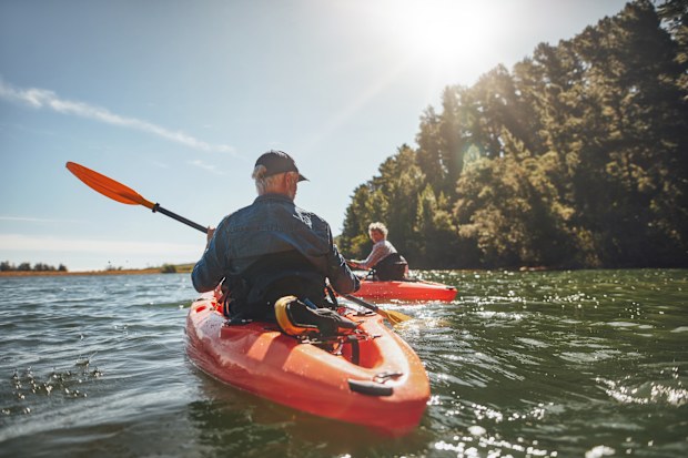 Outdoor shot of mature man canoeing in the lake with woman in background. Couple kayaking in the lake on a sunny day.