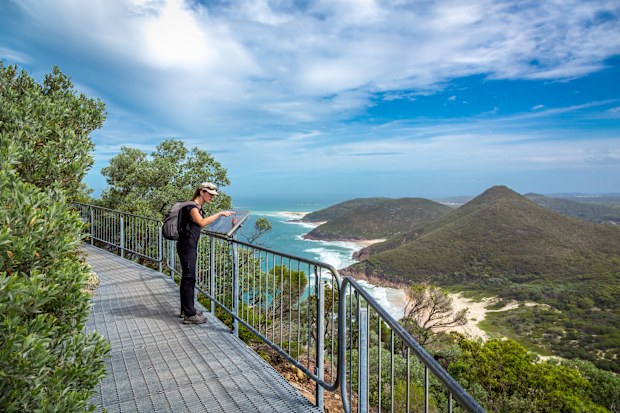 Woman Tourist wearing a backpack Looking at Map in Nelson Bay, Port Stephens, Australia. She is pointing the touristic map. The ocean and beaches are in the background.