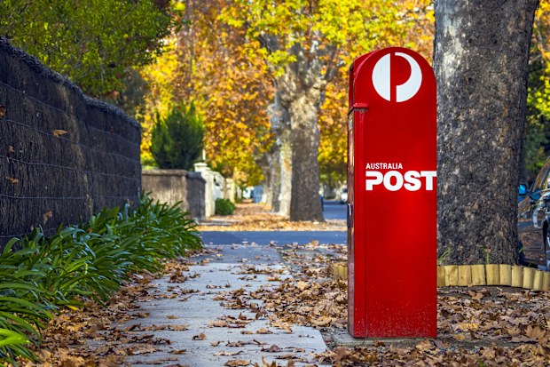 Adelaide, Australia - May 5, 2021: full length view of Australia Post Red Street Posting Box in quiet, leafy established suburban street. Autumn colours, brush fence, leaf litter, pavement, green plants