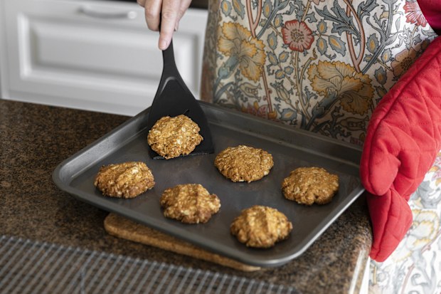 Homemade anzac biscuits being transferred onto a cooking rack.