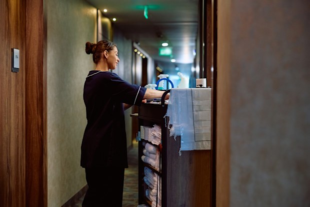 Smiling hotel housekeeper with chambermaid's trolley in hallway. Copy space.
