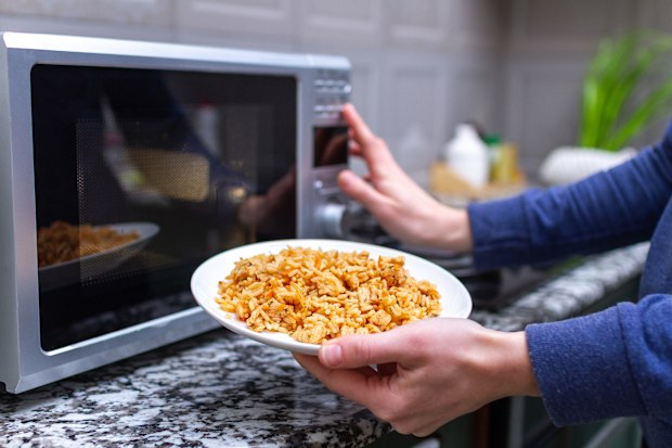 Using a microwave to warming a plate of homemade pilaf for lunch at home. Hot meal