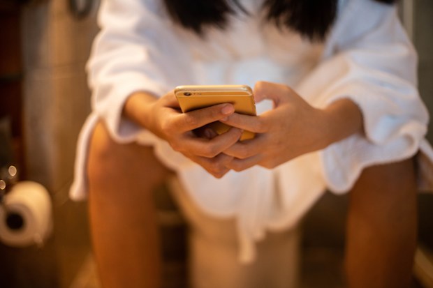 Woman scrolling her phone while on the toilet
