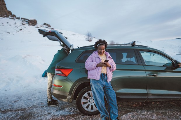 Photo of a young African American woman checking the maps on her mobile phone, while on a road trip with her car