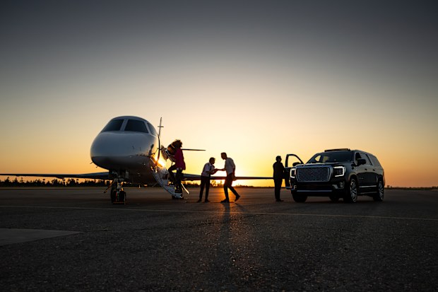 A young pilot welcomes passengers into private jet at dusk.