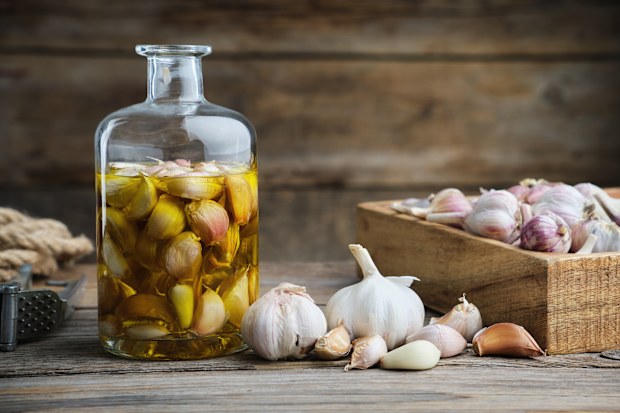Garlic aromatic flavored oil or infusion bottle, wooden crate of garlic cloves and  garlic press on wooden kitchen table.
