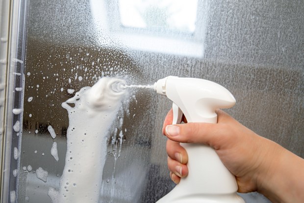 Person hand using limescale remover chemical foam. Descaling shower case glass door. Work in progress.