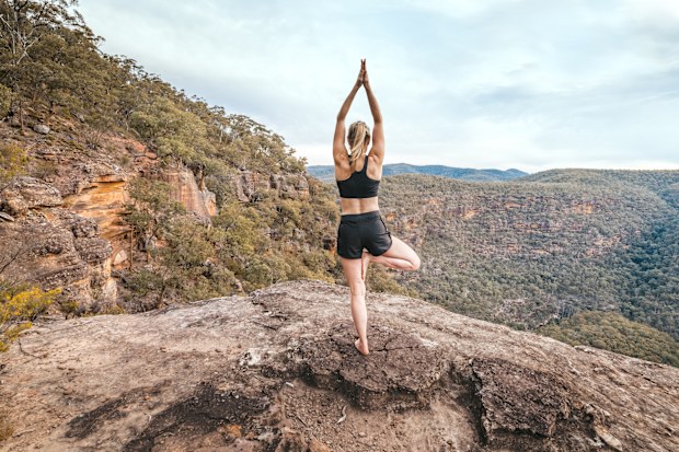 Female yoga exercise fitness.  She is balancing on one leg standing on a cliff ledge overlooking the gorge junctions. Wollemi National Park