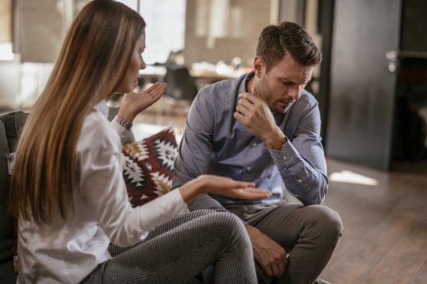 Unhappy young couple. Woman seems to be speaking while man looks down at ground.