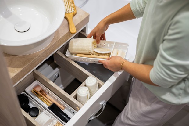 Top view of woman hands neatly organising bathroom amenities and toiletries in drawer or cupboard in bathroom. Concept of tidying up a bathroom storage by using Marie Kondo's method.