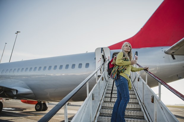 One mature woman is standing on the air-stair of her plane with her boarding pass and has turned round to give one last look to her home before she goes travelling.