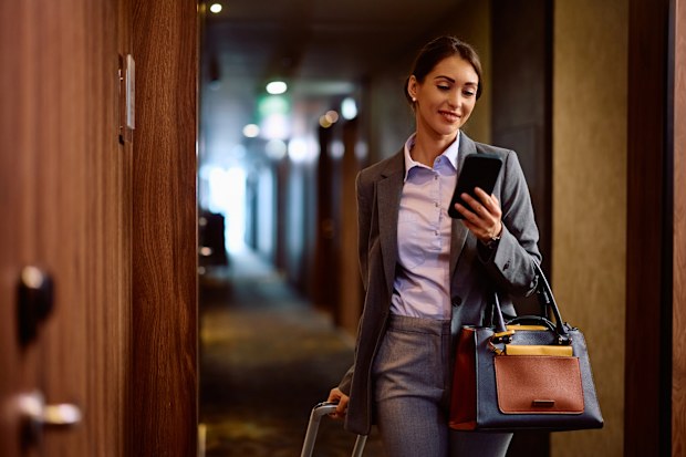 Happy female entrepreneur text messaging on cell phone while walking through hotel hallway. Copy space.