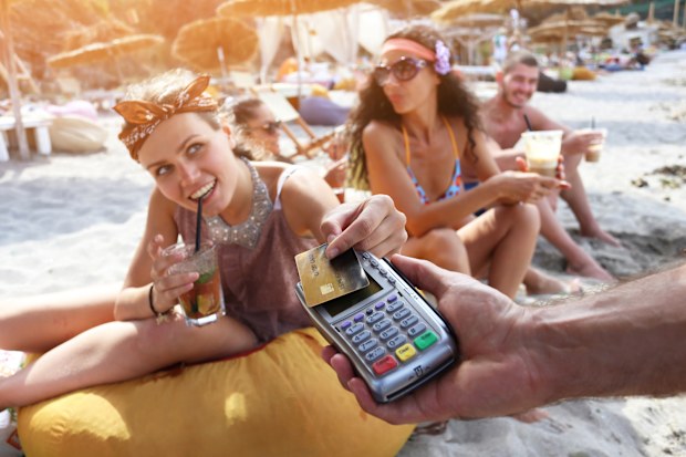 Cheerful friends drinking cocktails on beach and using credit card for payment.